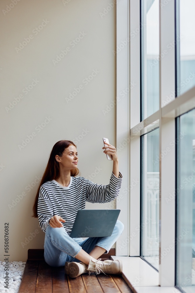 Freelance woman sitting with laptop and phone at window, video phone call, happiness of work online Freelance woman sitting with laptop and phone at window, video phone call, happiness of work online
