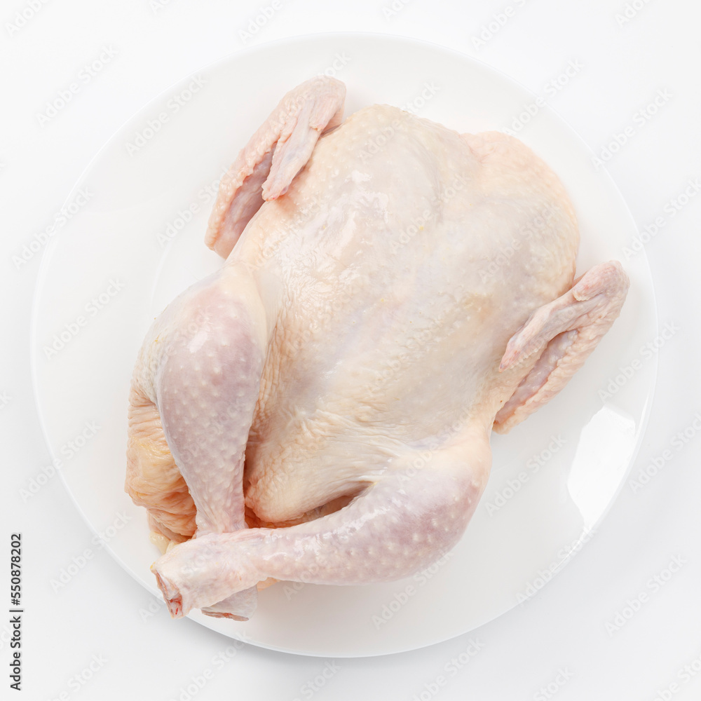 A whole raw chicken carcass on a white plate. A whole raw chicken carcass on a white plate.
