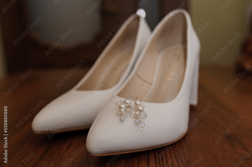 Earrings with pearls on white women's leather shoes. Bride's accessories, bride's morning Earrings with pearls on white women's leather shoes. Bride's accessories, bride's morning