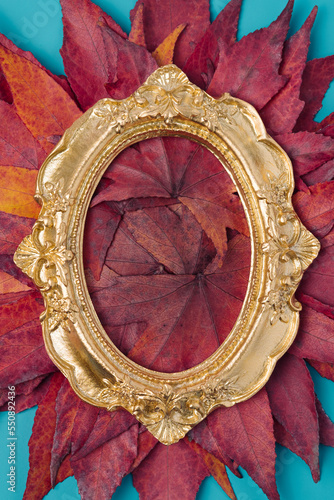 Vintage golden oval frame on a dry red maple leaves. Retro, natural minimal background. © Neeqolah