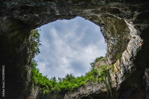 Low-angle view through a rocky hole to the blue sky over the greenery photo