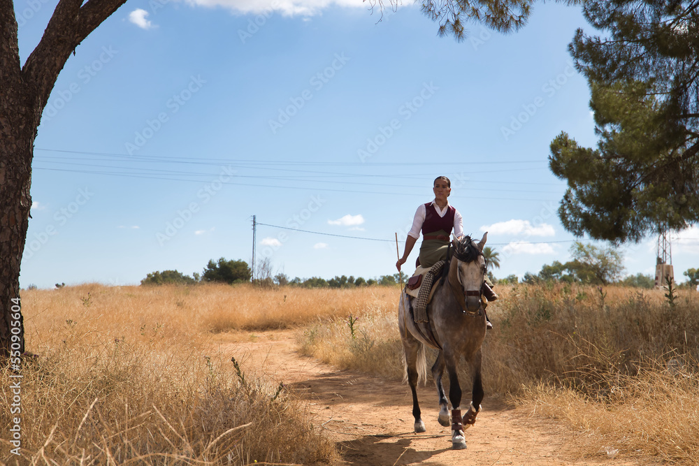 Woman horsewoman, young and beautiful, walking with her horse, in the countryside surrounded by dry grass. Concept horse riding, animals, dressage, horsewoman, cowgirl.