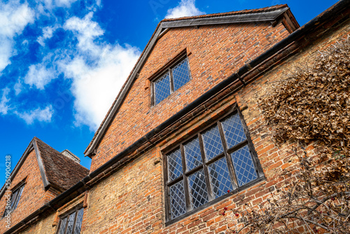 Vertical aspect of a Tudor-built home seen within the grounds of an English castle. The fine design is seen against a near clear blue sky.
