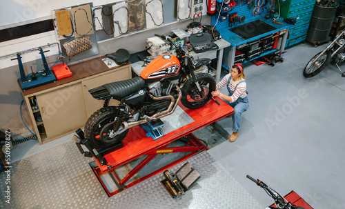 Top view of mechanic woman reviewing custom motorcycle over platform on factory