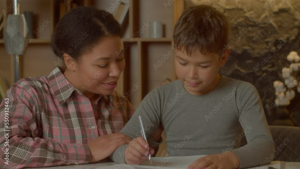 Portrait of affectionate charming black asian mother talking and sharing with cute elementary age multiethnic son, expressing support and care while smart schoolboy learning in domestic room. Portrait of affectionate charming black asian mother talking and sharing with cute elementary age multiethnic son, expressing support and care while smart schoolboy learning in domestic room.