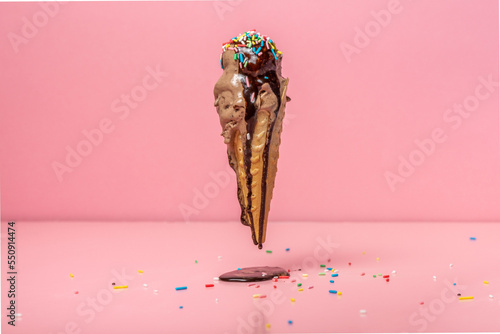 funny creative concept of flying wafer cone with ice cream covered, strewed sprinkles and poured with chocolate icing on pink background photo