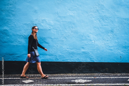 Young woman walks on street against blue wall, Ponta Delgada, Azores photo