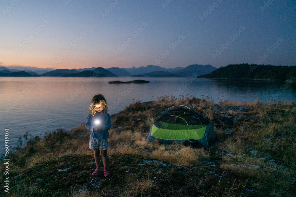 A young girl with a flashlight camping on a rocky island A young girl with a flashlight camping on a rocky island