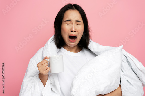 Yawning asian girl holding cup of morning coffee and trying to wake up