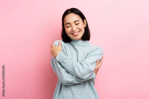 Fototapeta Portrait of self-satisfied egoistic woman embracing herself and smiling with ple