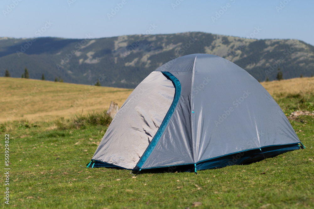 A gray tent standing in a clearing against the backdrop of mountains.