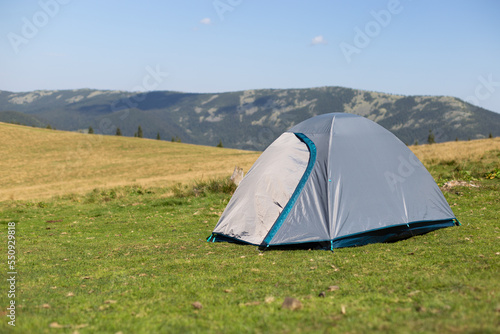 A gray tent standing in a clearing against the backdrop of mountains.