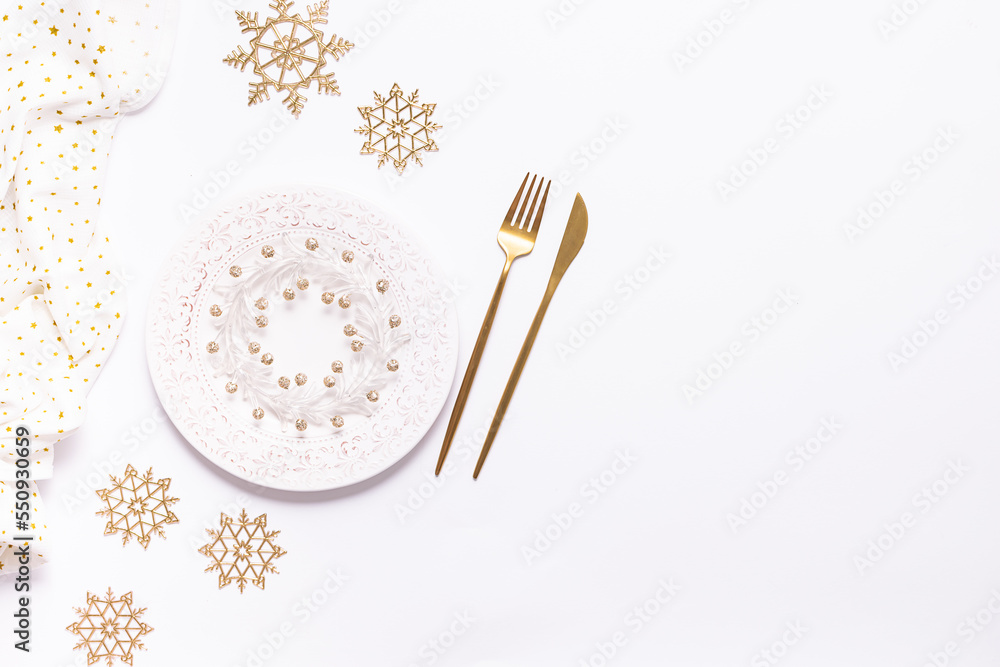 Festive Christmas table setting with white plate with ornament, golden cutlery set and decorative snow flakes on white background with copy space for your design. Festive Christmas table setting with white plate with ornament, golden cutlery set and decorative snow flakes on white background with copy space for your design.