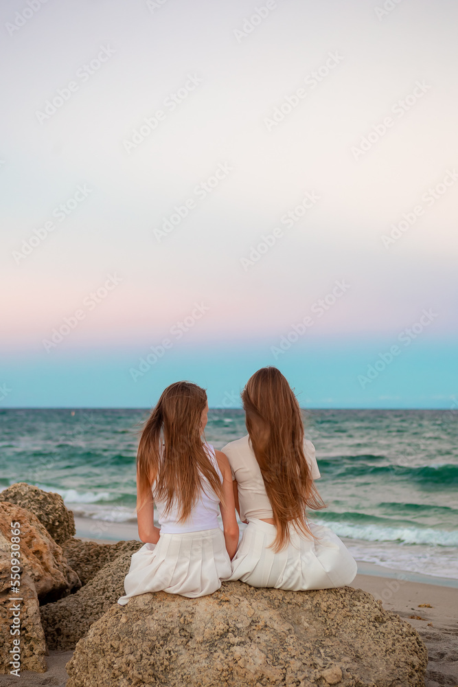 Adorable girls with long hair enjoy the view of the sea on the beach at sunset Adorable girls with long hair enjoy the view of the sea on the beach at sunset