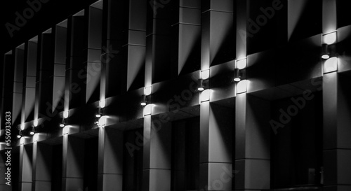 Grayscale exterior shot of modern facade with pattern poles wotj illuminated lights photo