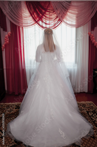 A girl in a white wedding dress at the window. Bride in a dress at the window