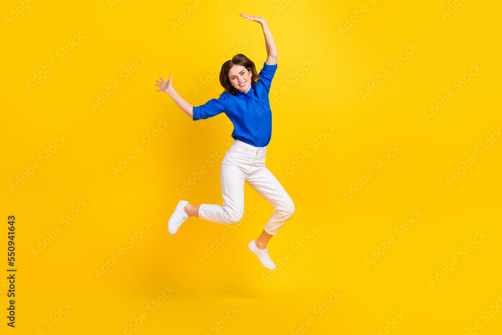Full length photo of pretty adorable lady wear blue shirt jumping high rising hands arms isolated yellow color background