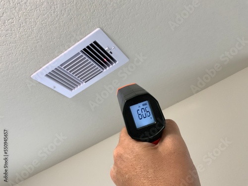 Measuring air conditioning flow temperature on a white ceiling register with a digital laser thermometer