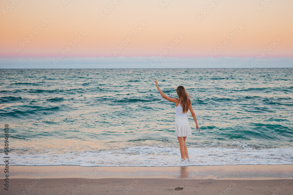 Adorable happy girl on the beach at sunset walking in shallow water Adorable happy girl on the beach at sunset walking in shallow water