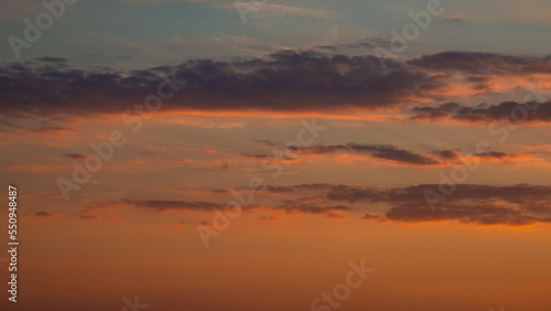 Soft deep orange sky, illuminated clouds at bloody sunset as a background.