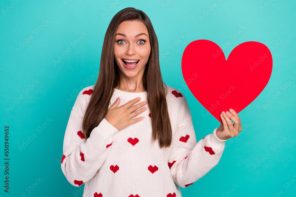 Photo of astonished positive girl hold large red paper heart hand touch chest isolated on emerald color background