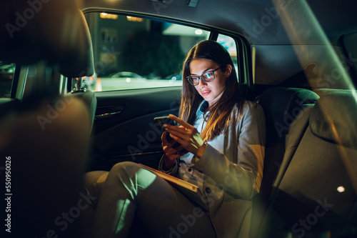 Photo Business woman using smartphone while sitting in a backseat of a car at night