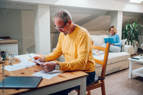 Senior man sitting at table and looking into blueprints of his new home