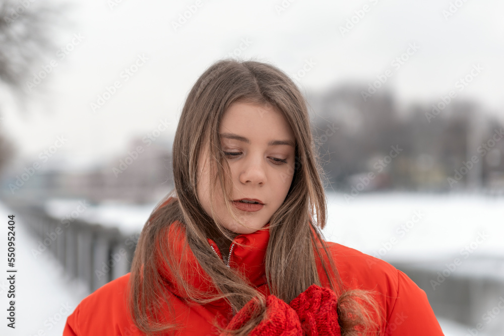 Portrait of beautiful girl in red jacket and red knitted mittens. Young woman in warm clothes outdoors in winter park Portrait of beautiful girl in red jacket and red knitted mittens. Young woman in warm clothes outdoors in winter park
