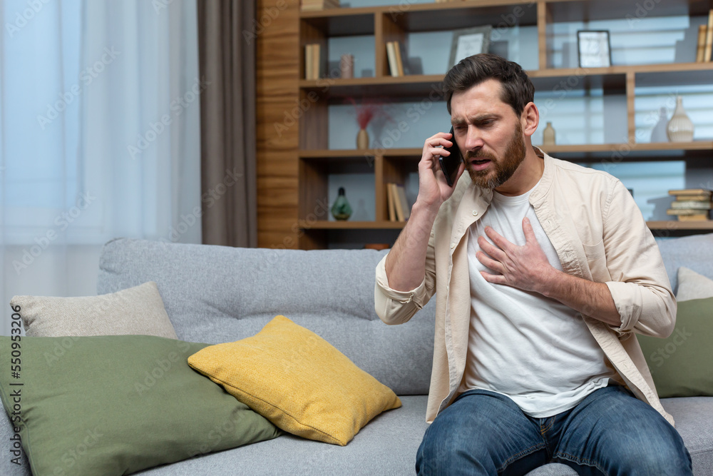 Man having heart attack at home, patient calling doctor using phone, sitting on couch in living room at home. Man having heart attack at home, patient calling doctor using phone, sitting on couch in living room at home.