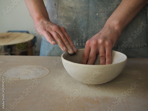 Unrecognizable woman ceramist peeling a clay plate holding sponge. The process of irregularities and grinding of the finished product. Small business, hobby, ceramic concept.