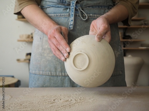Unrecognizable woman ceramist peeling a clay plate holding sponge. The process of irregularities and grinding of the finished product. Small business, hobby, ceramic concept. photo