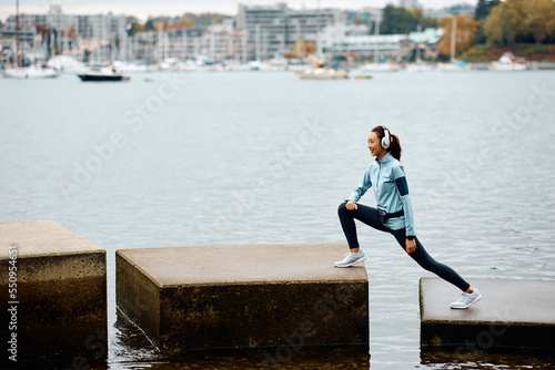 Happy Asian female athlete doing stretching exercise by water.