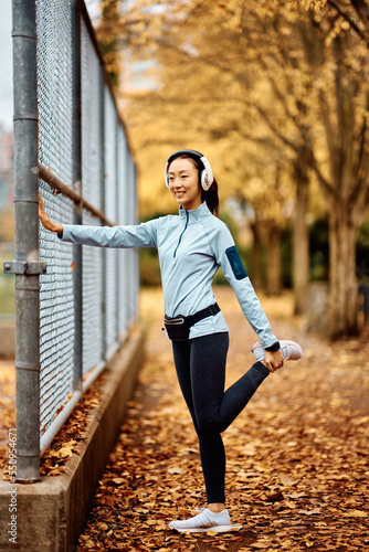 Happy Asian female runner warming up in park.