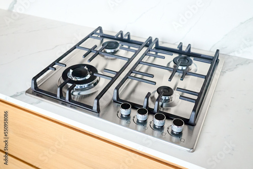 Modern hob gas or gas stove made of stainless steel using natural gas or propane for cooking products on light stoneware countertop in kitchen interior with copyspace.
