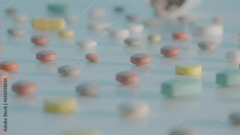 Various medical pills, capsules and tablets scattered on a table on a blue background with different depth of field. Brown, white and yellow medicines close up. Slow motion ready 59.94fps. Various medical pills, capsules and tablets scattered on a table on a blue background with different depth of field. Brown, white and yellow medicines close up. Slow motion ready 59.94fps.