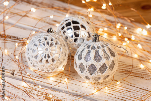 Christmas tree decorations. Silver balls are tied with handmade lace. A bright Christmas lights on a white wooden base