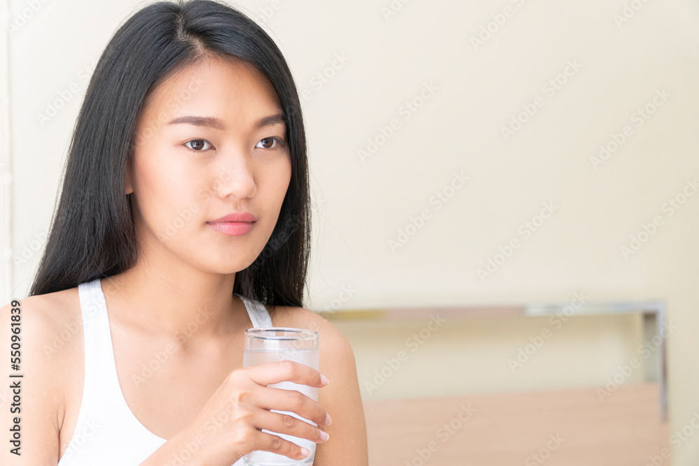 Positive asian women holding pure water glass drink after wake up at home. Beautiful young girl long hair after wake up drinking fresh water glass beverage in morning for healthy Lifestyle health care Positive asian women holding pure water glass drink after wake up at home. Beautiful young girl long hair after wake up drinking fresh water glass beverage in morning for healthy Lifestyle health care
