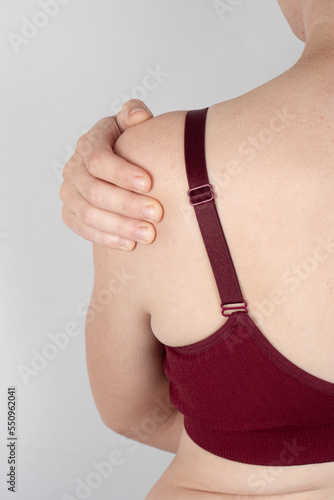 woman in a sports bra holding her sore shoulder, stretched tendons of the forearm.