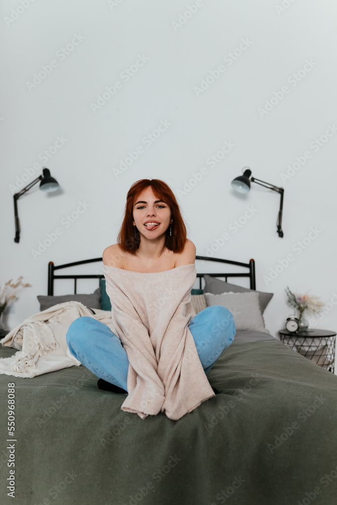 Young woman in casual clothes sitting on bed at home