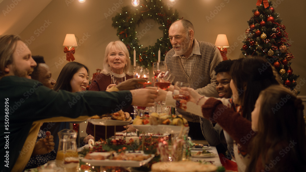 Happy multi cultural family celebrating Christmas or New Year, raising glasses with wine. Served holiday table with dishes and candles. Warm atmosphere of family Christmas dinner at home. Cheers. Happy multi cultural family celebrating Christmas or New Year, raising glasses with wine. Served holiday table with dishes and candles. Warm atmosphere of family Christmas dinner at home. Cheers.