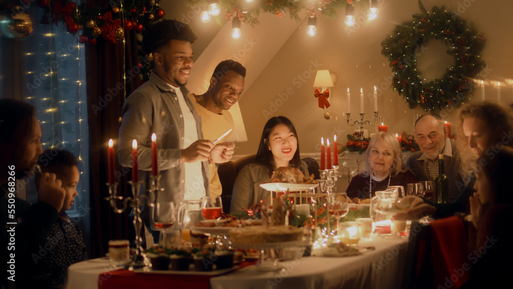 African American man cuts turkey with knife. Multi cultural family celebrating Christmas or New Year. Served holiday table with dishes and candles. Warm atmosphere of family Christmas dinner at home.