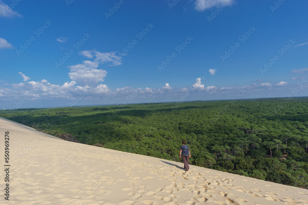 Tourist standing on Dune du Pilat, the biggest sand dune in Europe with the pine forest and view at the sea, Arcachon, Nouvelle-Aquitaine, France
