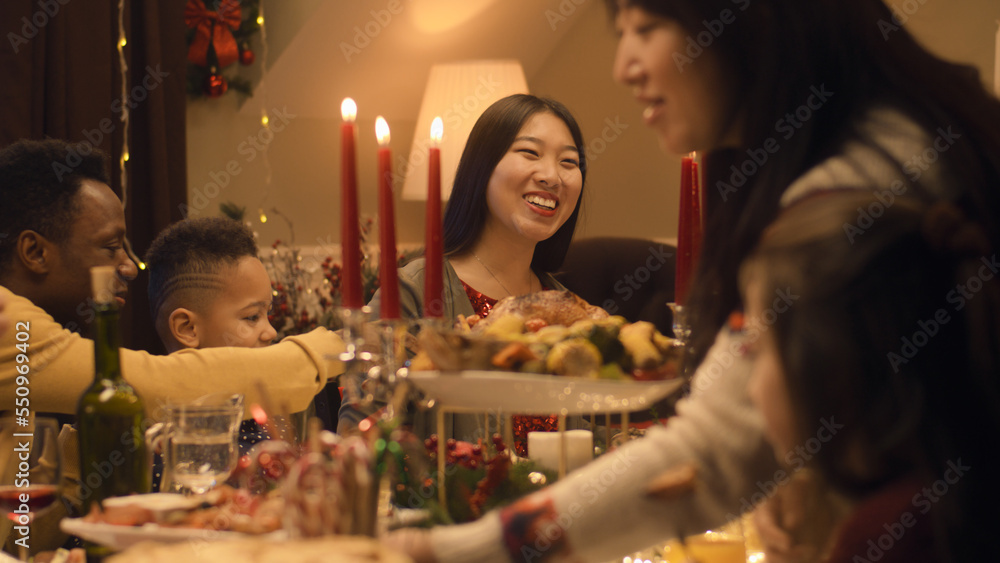 Happy multi cultural family celebrating Christmas or New Year 2023, talking and eating. Served holiday table with different dishes and candles. Warm atmosphere of family Christmas dinner at home. Happy multi cultural family celebrating Christmas or New Year 2023, talking and eating. Served holiday table with different dishes and candles. Warm atmosphere of family Christmas dinner at home.