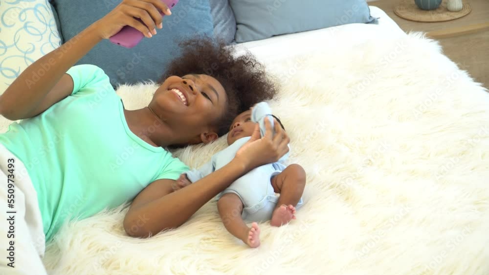 Young mother African American and newborn baby making video call and smiling greet. Happy elder sister taking Selfie with little brother infant curious lying on bed looking at mobile phone smiling. Young mother African American and newborn baby making video call and smiling greet. Happy elder sister taking Selfie with little brother infant curious lying on bed looking at mobile phone smiling.