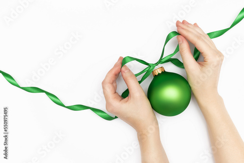 Fototapeta Naklejka Na Ścianę i Meble -  Merry Christmas concept greeting card. Women s hands tying a bow on the green christmas ball