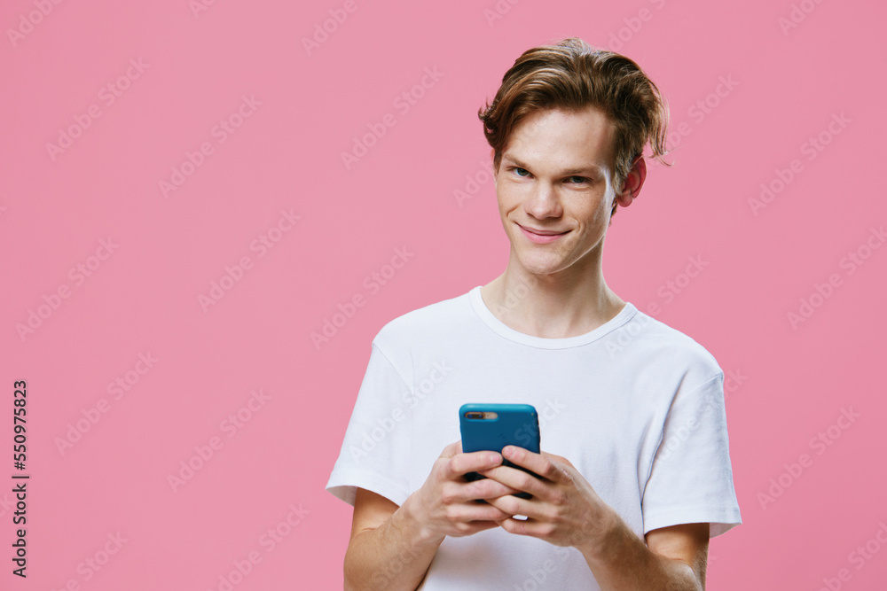 handsome, pleasant red-haired guy in a white t-shirt, writes messages on the phone, smiling at the camera handsome, pleasant red-haired guy in a white t-shirt, writes messages on the phone, smiling at the camera