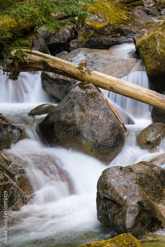 Mountain stream cascade over large boulders, a worn trees hang up on a rock above the silky fresh water photo