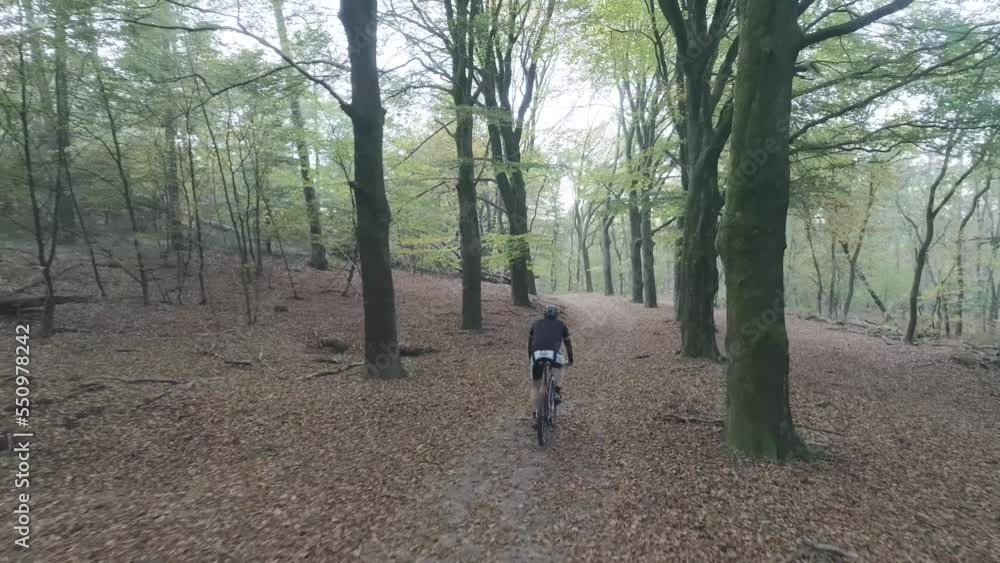 Behind drone shot of mountainbiker riding through forest. Behind drone shot of mountainbiker riding through forest.