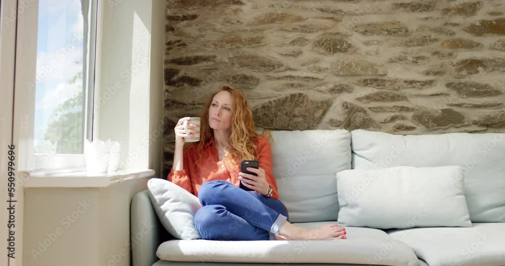 Phone, coffee and woman relax on a sofa, thinking and searching online streaming app against wall background. Smartphone, tea and girl on a couch for social media, internet and search in living room Phone, coffee and woman relax on a sofa, thinking and searching online streaming app against wall background. Smartphone, tea and girl on a couch for social media, internet and search in living room