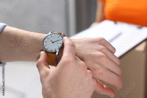 Closeup view of man checking time near courier with parcels indoors